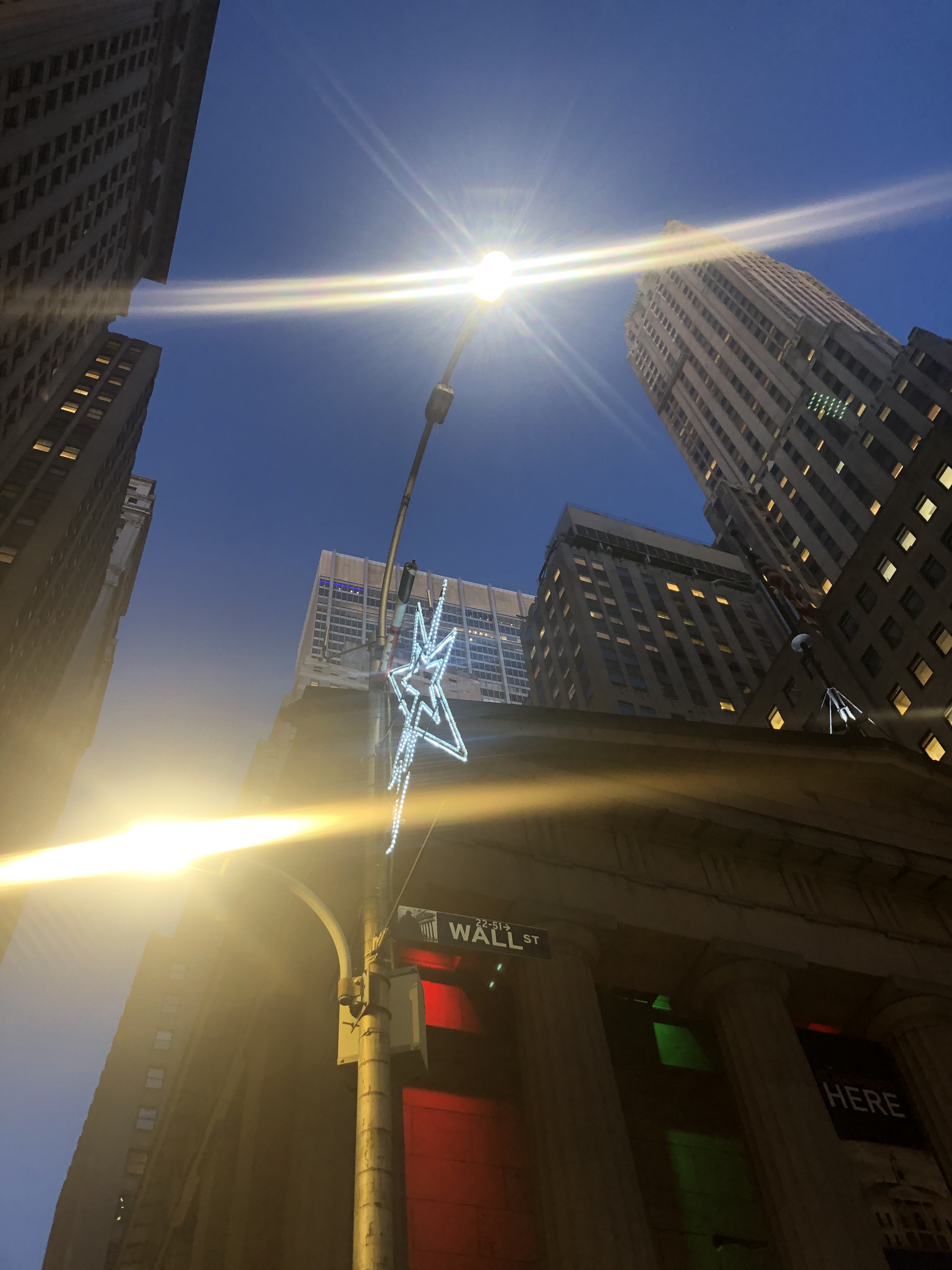 Star-shaped Christmas lights attached to a light pole near a Wall Street street sign